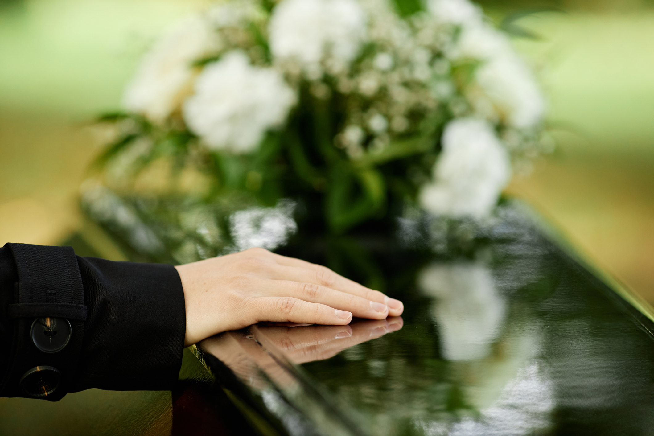 Close up of female hand on coffin saying goodbye at outdoor funeral ceremony