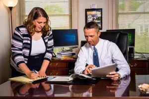 Bradley E. Holuta at his desk with secretary reviewing documents