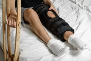 Female patient with orthosis holding crutches on bed after leg surgery, focusing on rehabilitation at home