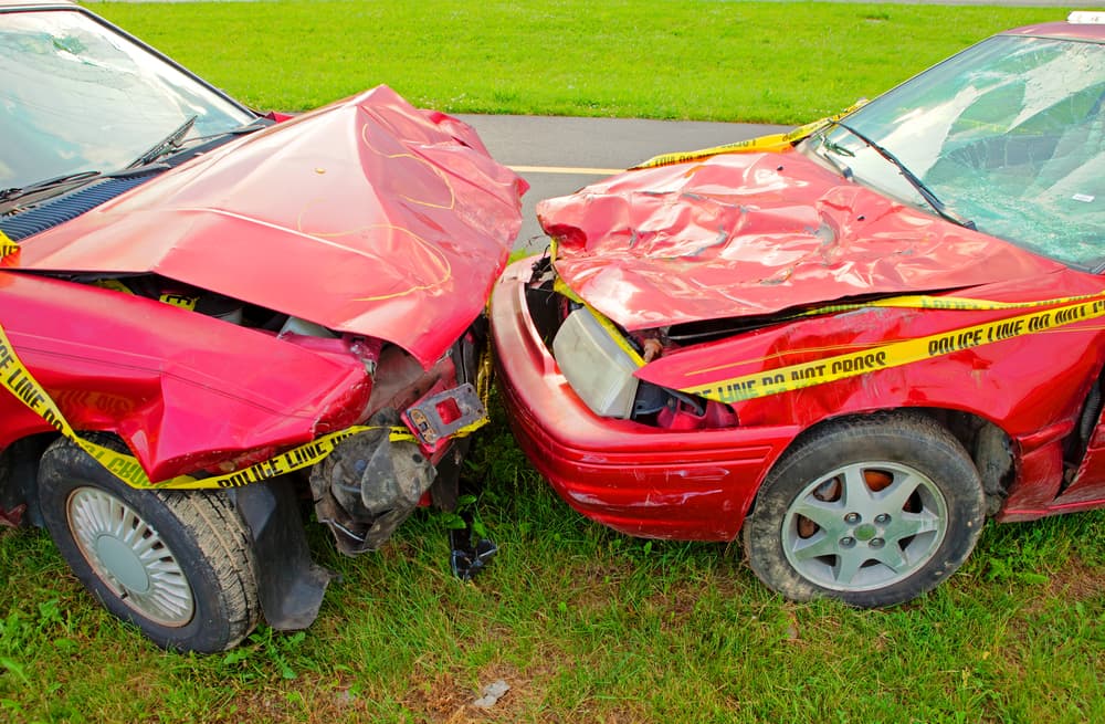 Two red cars with cracked windshields and smashed hoods after a head-on collision.