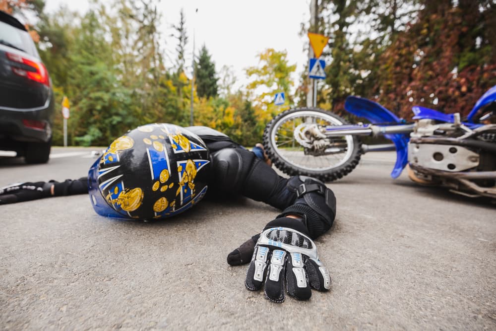 Biker in leather suit and helmet lying on road after accident