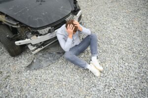 Young white man holding his head in pain near a broken car on the road after head-on collision.