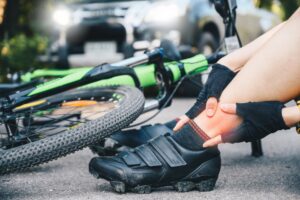 Cyclist woman experiencing ankle pain after a car accident on the road, highlighting the concept of car-bicycle collisions.