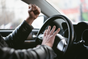 An angry driver is honking and yelling while sitting behind the steering wheel, illustrating road rage during a traffic jam.