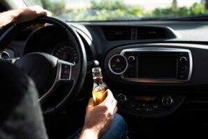 A driver holding a bottle of alcohol while driving